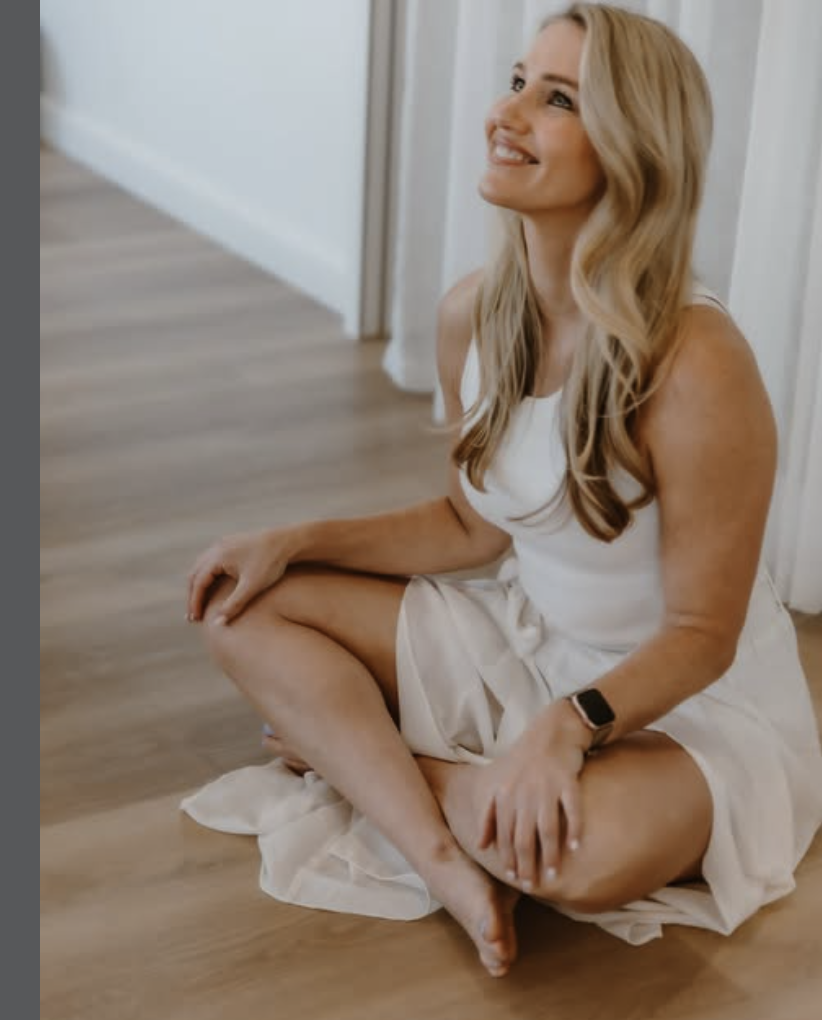 Zoe seated cross-legged, smiling — light-filled wooden studio